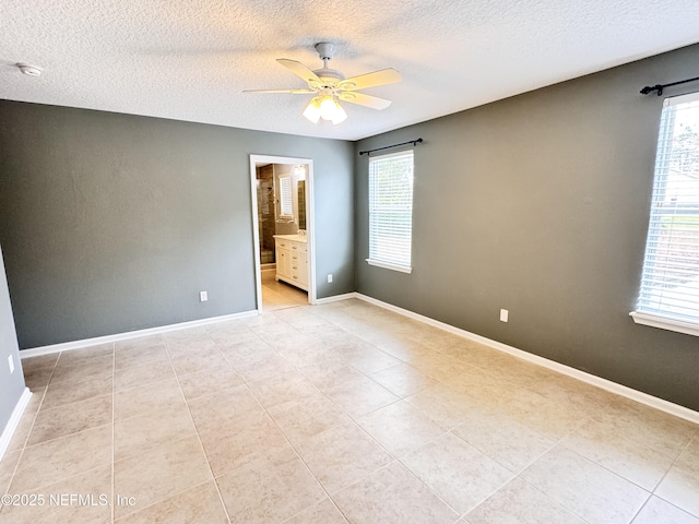 empty room with a wealth of natural light, a textured ceiling, a ceiling fan, and baseboards