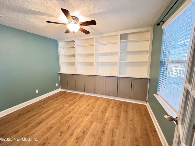 interior space with light wood finished floors, a textured ceiling, baseboards, and a ceiling fan