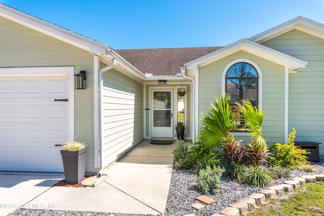 view of exterior entry featuring an attached garage and a shingled roof