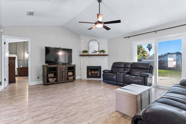 living room featuring light wood finished floors, a large fireplace, visible vents, lofted ceiling, and ceiling fan