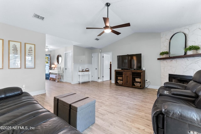 living room featuring visible vents, lofted ceiling, light wood-style flooring, ceiling fan, and a stone fireplace