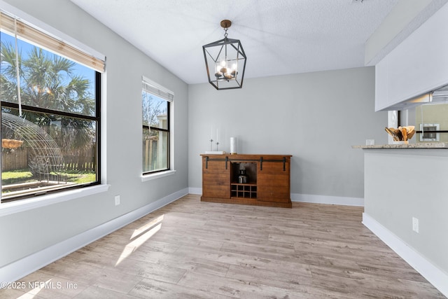 unfurnished office featuring light wood-style flooring, baseboards, and an inviting chandelier