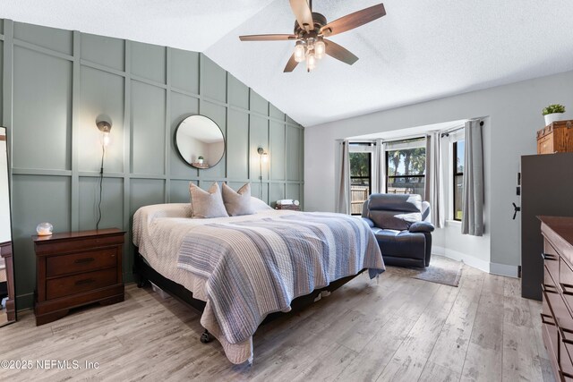 bedroom featuring lofted ceiling, ceiling fan, a textured ceiling, a decorative wall, and light wood-type flooring