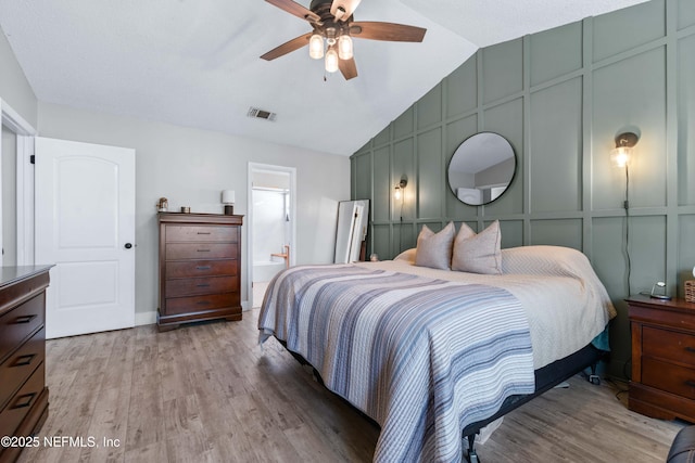 bedroom with light wood-type flooring, visible vents, a decorative wall, and lofted ceiling