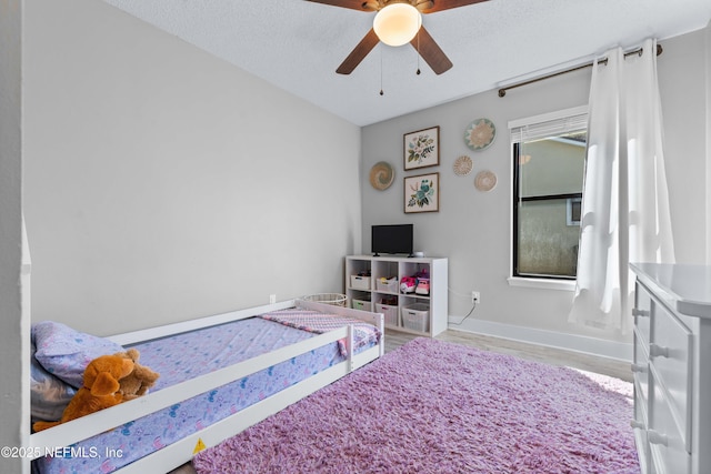 bedroom with ceiling fan, a textured ceiling, baseboards, and wood finished floors