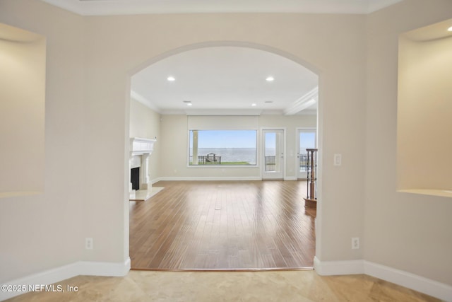 unfurnished living room with arched walkways, a fireplace, wood finished floors, baseboards, and ornamental molding