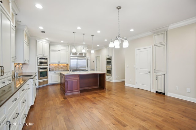 kitchen with stainless steel appliances, wood finished floors, a sink, visible vents, and crown molding