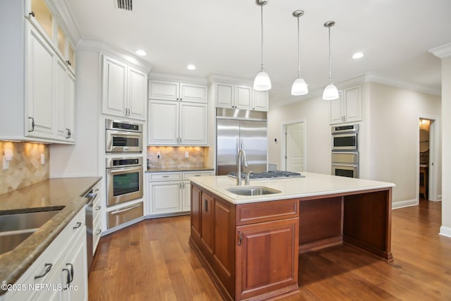 kitchen with dark wood-style floors, a warming drawer, appliances with stainless steel finishes, a sink, and an island with sink