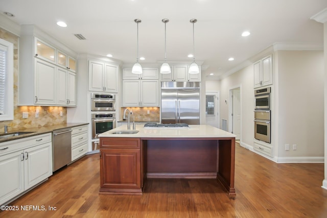 kitchen featuring dark wood-type flooring, a sink, visible vents, appliances with stainless steel finishes, and a center island with sink