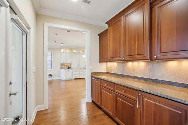 kitchen with light wood-style floors, stone counters, decorative backsplash, and brown cabinetry