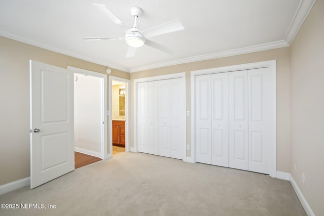 unfurnished bedroom featuring light colored carpet, baseboards, multiple closets, ornamental molding, and ensuite bath