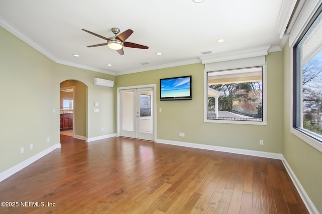 empty room with arched walkways, ornamental molding, wood finished floors, a wall mounted air conditioner, and baseboards