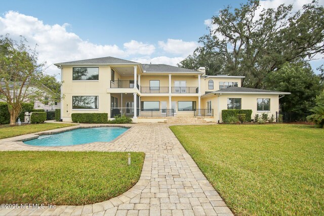 back of house with an outdoor pool, a balcony, a yard, a patio area, and stucco siding