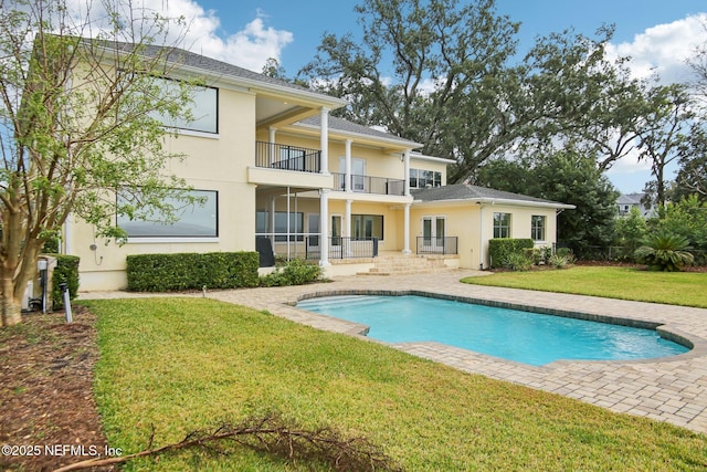 back of house with a yard, an outdoor pool, a balcony, and stucco siding