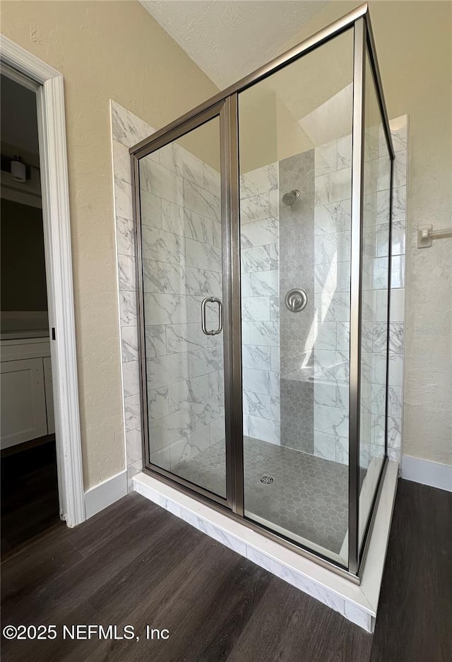 bathroom featuring a textured wall, a shower stall, baseboards, and wood finished floors