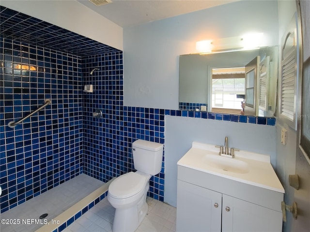 full bath with toilet, tile patterned floors, a tile shower, vanity, and tile walls