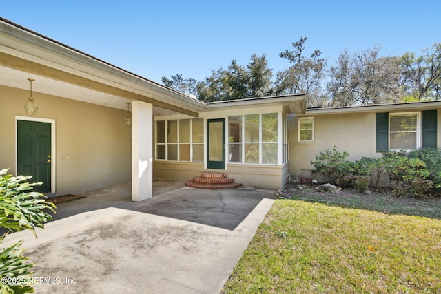 entrance to property featuring a patio area, a lawn, and stucco siding