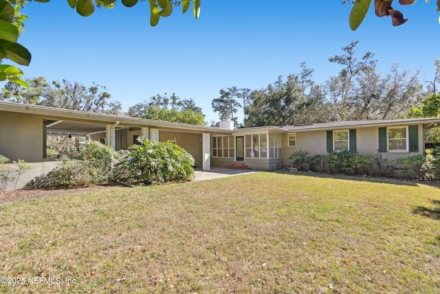 ranch-style home featuring a sunroom, a chimney, stucco siding, and a front yard