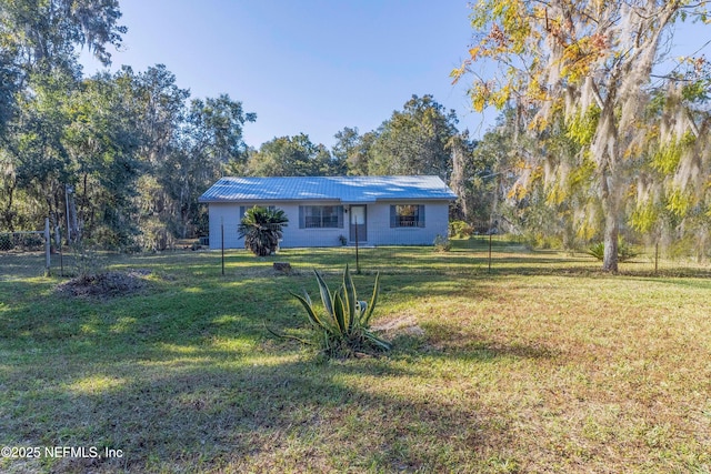 view of front of property featuring metal roof, concrete block siding, a front yard, and fence