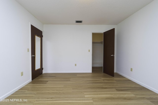 unfurnished room with visible vents, light wood-style flooring, a textured ceiling, and baseboards