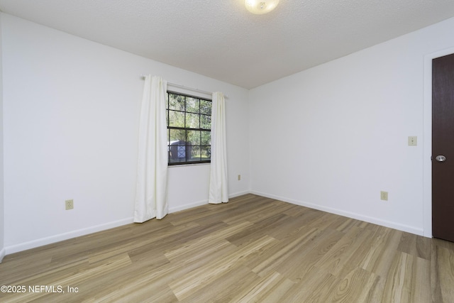 spare room with baseboards, a textured ceiling, and light wood finished floors