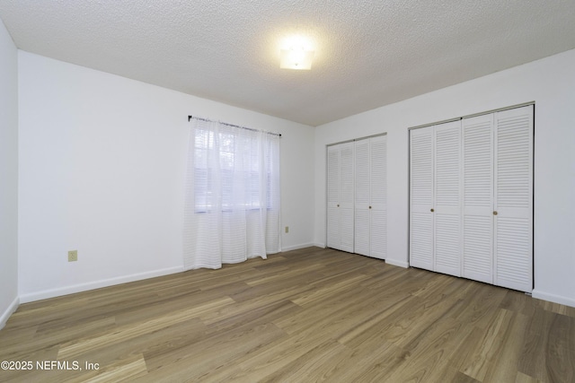 unfurnished bedroom with light wood-type flooring, baseboards, two closets, and a textured ceiling