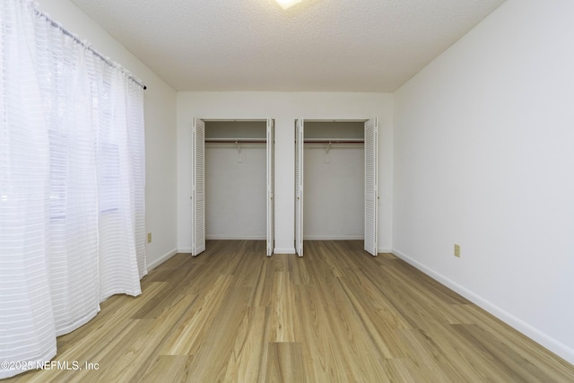 unfurnished bedroom with a textured ceiling, baseboards, two closets, and light wood finished floors