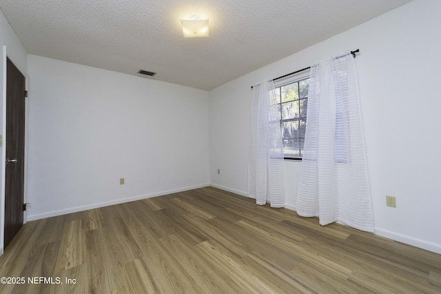 empty room featuring visible vents, baseboards, a textured ceiling, and light wood-style flooring