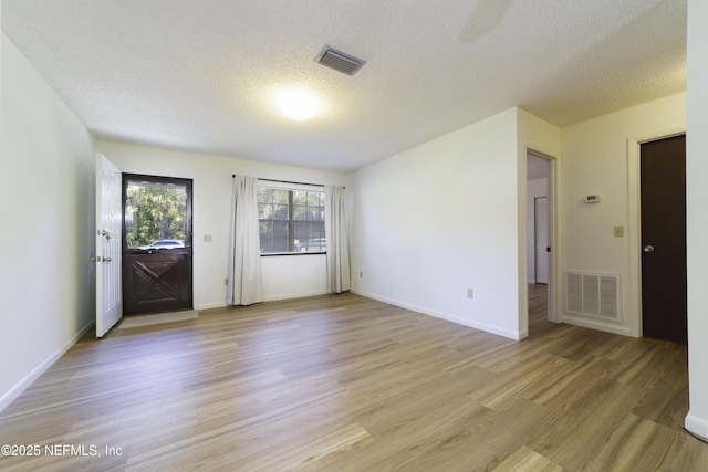 interior space featuring baseboards, light wood-style floors, visible vents, and a textured ceiling