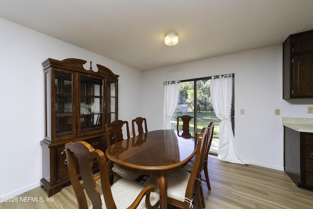 dining area with light wood-style flooring, baseboards, and a textured ceiling