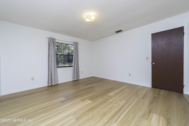 unfurnished room with baseboards, visible vents, light wood finished floors, and a textured ceiling