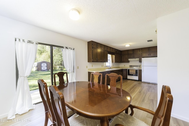 dining area featuring light wood-style flooring, visible vents, and a textured ceiling