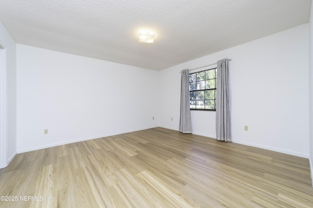 spare room with light wood-type flooring, baseboards, and a textured ceiling