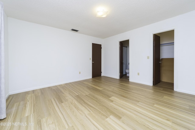 unfurnished bedroom featuring baseboards, visible vents, light wood-style floors, a textured ceiling, and a walk in closet