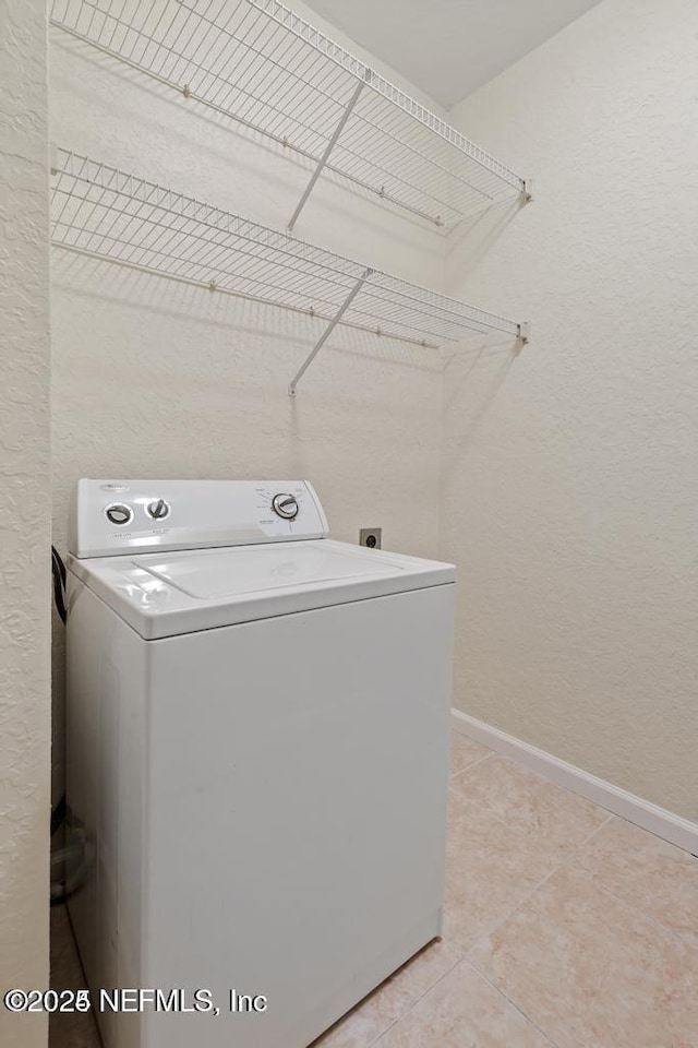 clothes washing area featuring laundry area, baseboards, a textured wall, washer / clothes dryer, and light tile patterned flooring