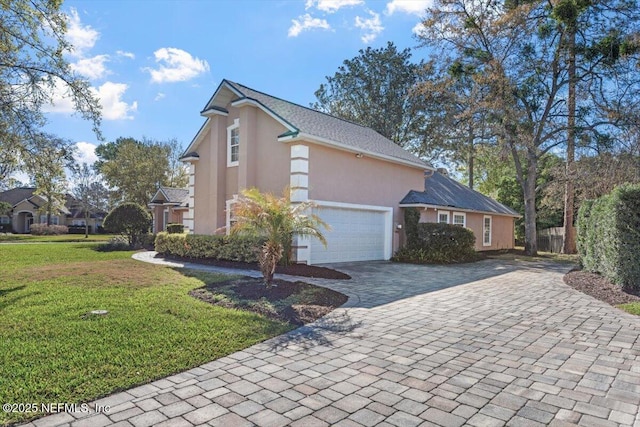 view of side of property featuring an attached garage, a yard, decorative driveway, and stucco siding