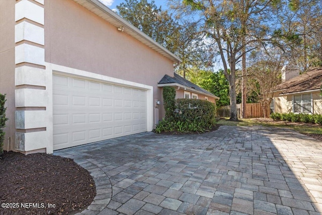 view of property exterior with decorative driveway, fence, an attached garage, and stucco siding