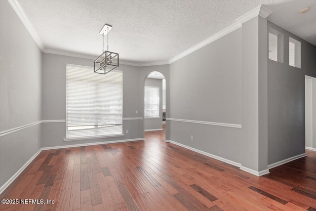 unfurnished dining area featuring arched walkways, a textured ceiling, baseboards, ornamental molding, and wood-type flooring