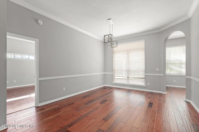 empty room with baseboards, a textured ceiling, ornamental molding, and wood finished floors