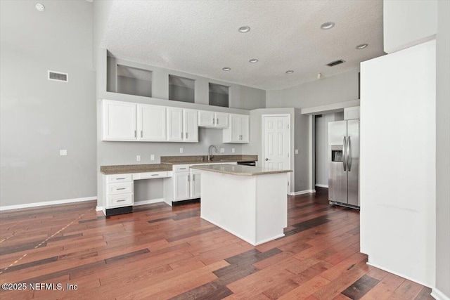 kitchen featuring dark wood finished floors, stainless steel refrigerator with ice dispenser, visible vents, white cabinets, and a sink