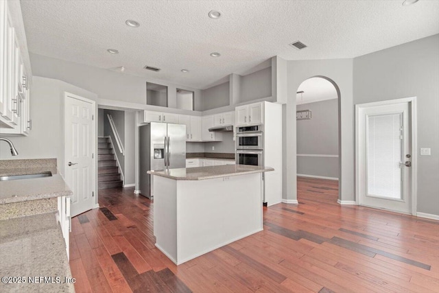 kitchen featuring visible vents, arched walkways, appliances with stainless steel finishes, hardwood / wood-style floors, and a sink