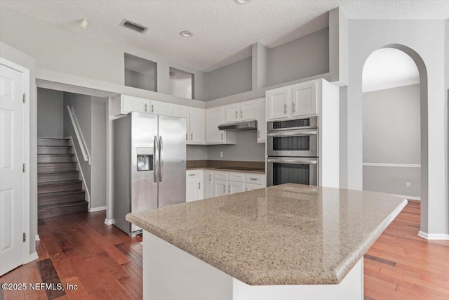 kitchen with under cabinet range hood, white cabinetry, visible vents, appliances with stainless steel finishes, and light stone countertops