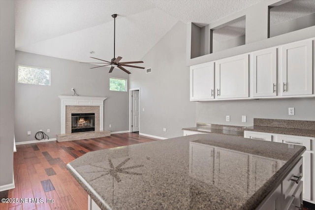 kitchen with a glass covered fireplace, white cabinets, plenty of natural light, and wood finished floors