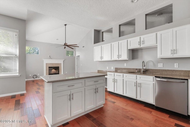 kitchen with dishwasher, a glass covered fireplace, lofted ceiling, wood finished floors, and a sink