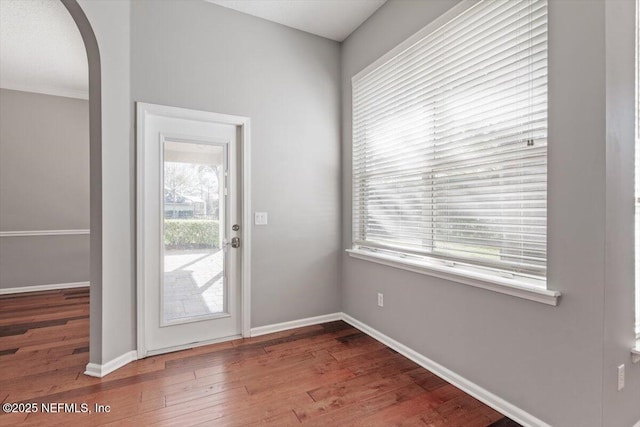 doorway to outside featuring arched walkways, wood-type flooring, and baseboards