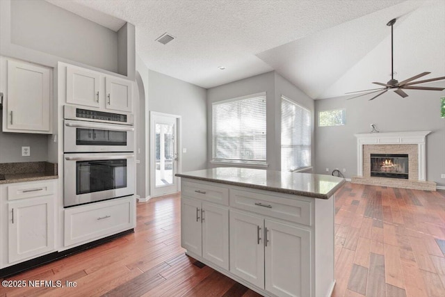 kitchen featuring double oven, white cabinets, vaulted ceiling, light wood finished floors, and a glass covered fireplace