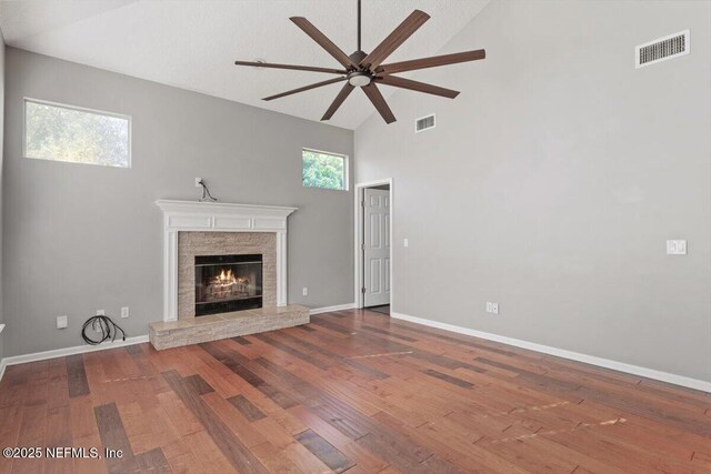 unfurnished living room featuring a stone fireplace, wood finished floors, visible vents, and baseboards