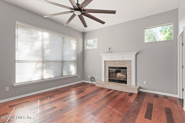 unfurnished living room featuring a stone fireplace, hardwood / wood-style flooring, a wealth of natural light, and baseboards