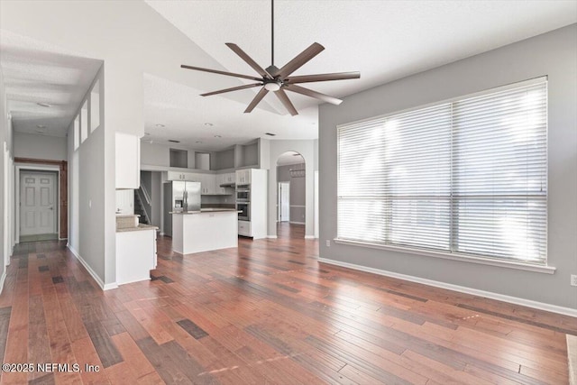 unfurnished living room with arched walkways, ceiling fan, dark wood finished floors, and baseboards