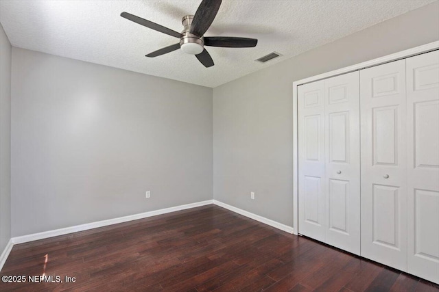 unfurnished bedroom featuring a closet, visible vents, a textured ceiling, wood finished floors, and baseboards